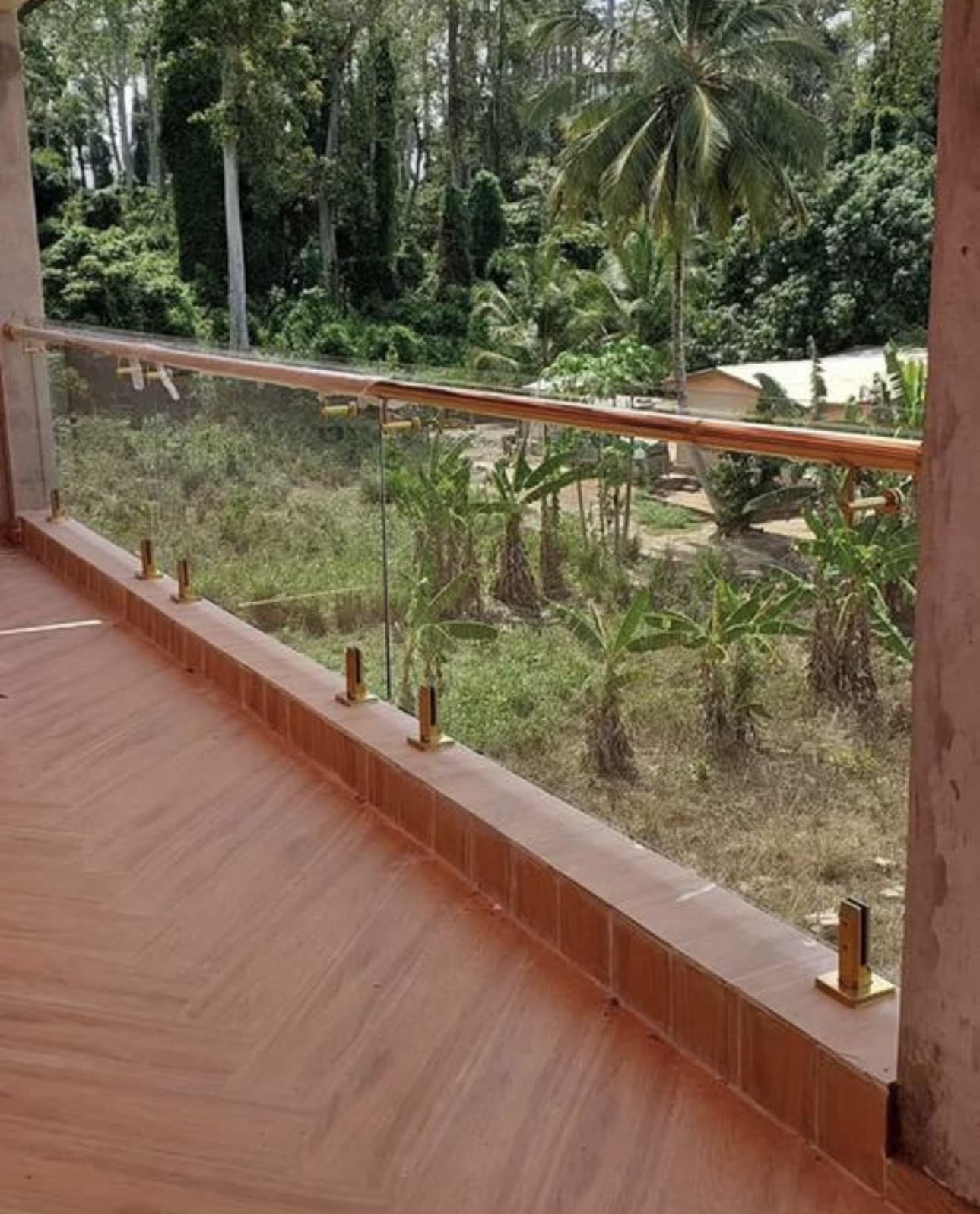 Outdoor terrace glass railing with gold spigots and wooden top rail